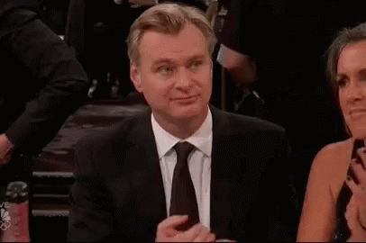 A Man In A Suit And Tie Is Sitting Next To A Woman In A Dress And Clapping . GIF
