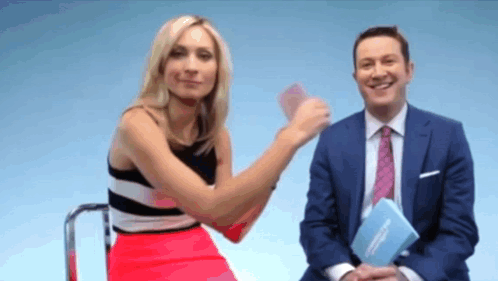 A Man In A Suit And Tie Is Sitting Next To A Woman In A Red Skirt GIF