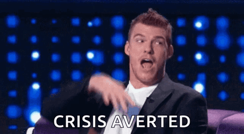 A Man In A Suit And Tie Is Sitting On A Couch And Making A Funny Face While Saying Crisis Averted GIF