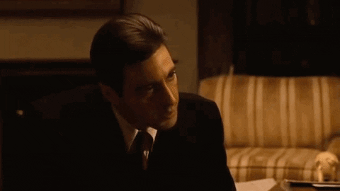 a man in a suit and tie is sitting on a couch and saying but your enemies closer .