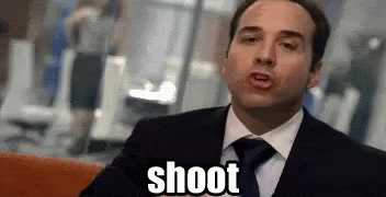 A Man In A Suit And Tie Is Sitting On A Couch And Says Shoot . GIF