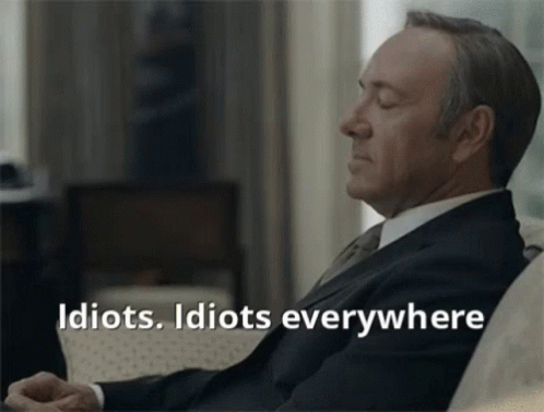 A Man In A Suit And Tie Is Sitting On A Couch With His Eyes Closed And The Words Idiots Idiots Everywhere Below Him GIF