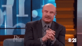 A Man In A Suit And Tie Is Sitting On A Couch With His Hands Folded GIF