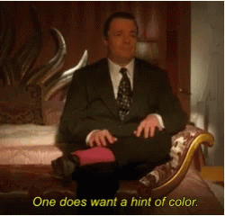 A Man In A Suit And Tie Is Sitting On A Couch With The Words One Does Want A Hint Of Color Below Him GIF