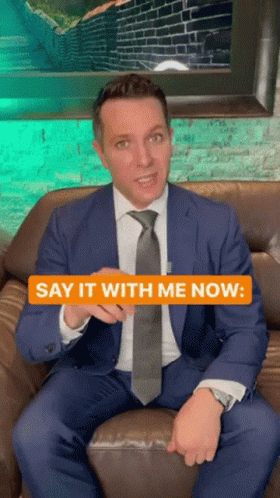 A Man In A Suit And Tie Is Sitting On A Couch With The Words Say It With Me Now GIF