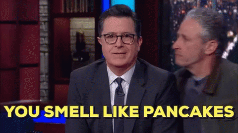 A Man In A Suit And Tie Is Sitting On A Stage And Says You Smell Like Pancakes . GIF