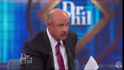 A Man In A Suit And Tie Is Sitting On A Stage In Front Of A Dr Phil Logo . GIF