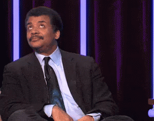 A Man In A Suit And Tie Is Sitting On A Stage With The Words `` Just Kidding '' Written On The Screen . GIF