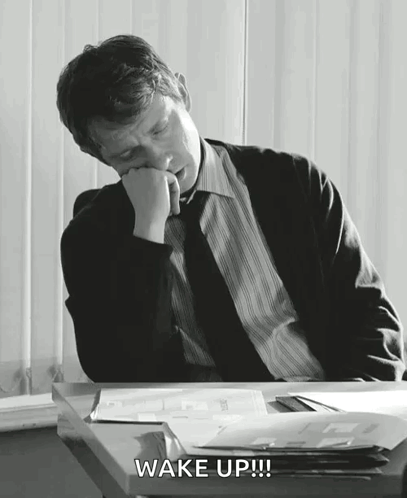 A Man In A Suit And Tie Is Sleeping At A Desk And The Words Wake Up Are Above Him GIF