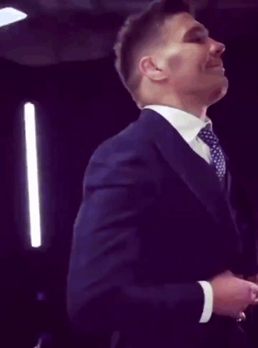 A Man In A Suit And Tie Is Smiling And Adjusting His Jacket GIF