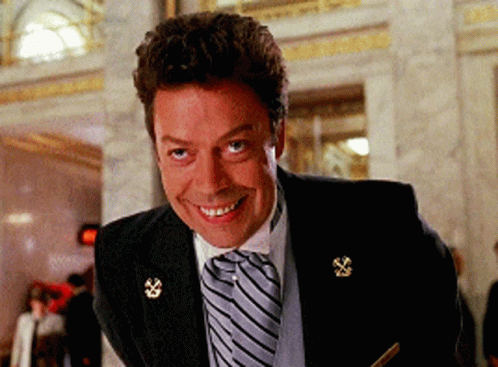 A Man In A Suit And Tie Is Smiling And Looking At The Camera GIF