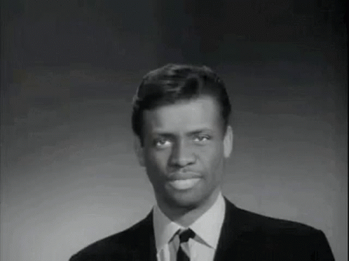 A Man In A Suit And Tie Is Smiling And Looking At The Camera . GIF