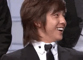 A Man In A Suit And Tie Is Smiling And Looking At The Camera . GIF