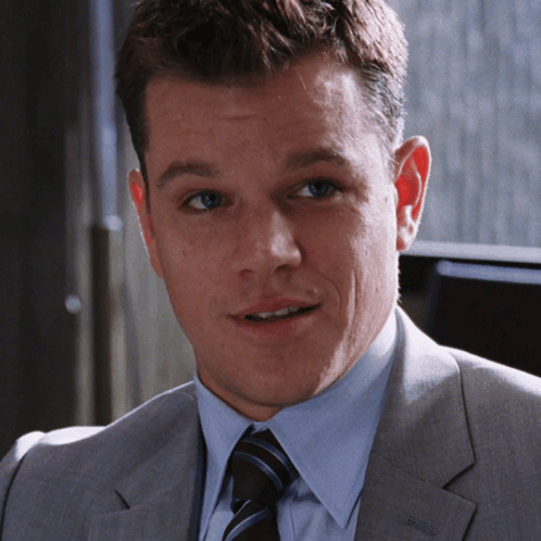 A Man In A Suit And Tie Is Smiling And Looking At The Camera GIF