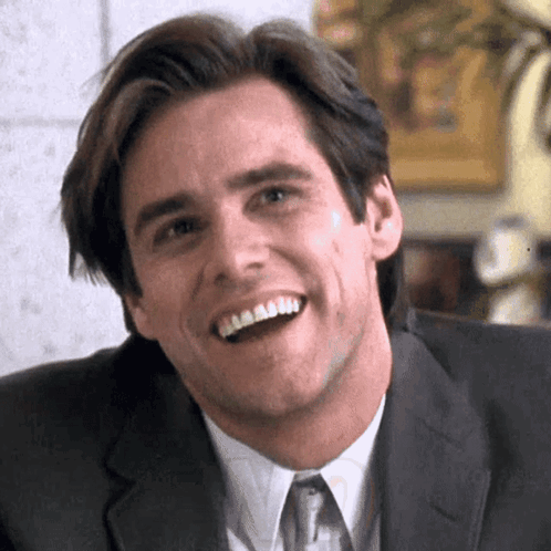 A Man In A Suit And Tie Is Smiling And Looking At The Camera . GIF