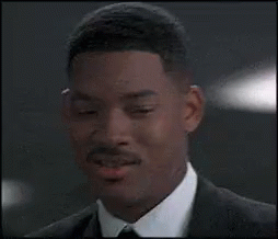 A Man In A Suit And Tie Is Smiling And Looking At The Camera . GIF