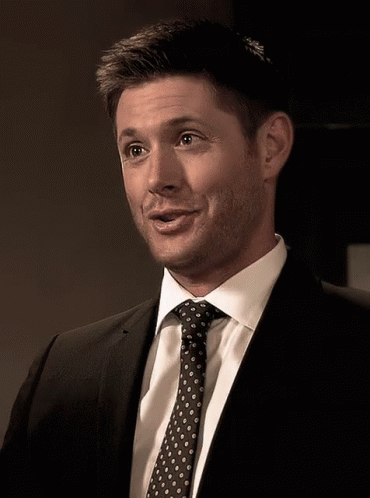 A Man In A Suit And Tie Is Smiling And Looking At The Camera GIF