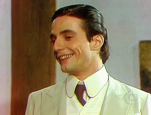 A Man In A Suit And Tie Is Smiling And Looking At The Camera GIF