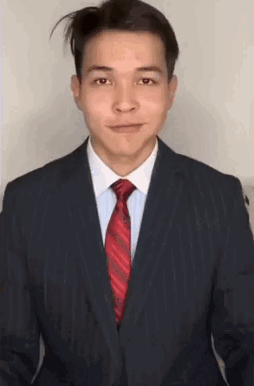 A Man In A Suit And Tie Is Smiling And Looking At The Camera . GIF