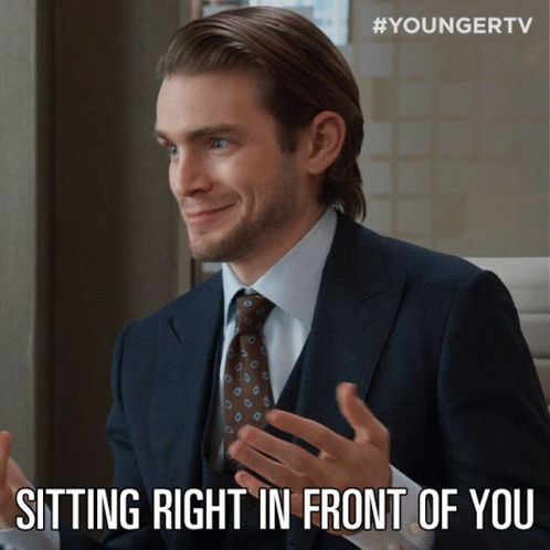 A Man In A Suit And Tie Is Smiling And Sitting Right In Front Of You GIF