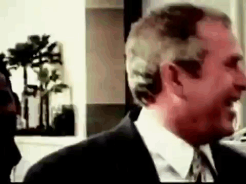 A Man In A Suit And Tie Is Smiling And Talking To Another Man . GIF