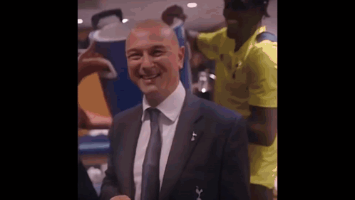 a man in a suit and tie is smiling for the camera while a man in a yellow shirt stands behind him .