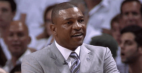 A Man In A Suit And Tie Is Smiling In Front Of A Crowd Of People GIF