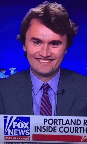 A Man In A Suit And Tie Is Smiling In Front Of A Fox News Banner GIF