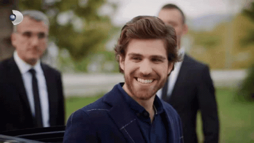 A Man In A Suit And Tie Is Smiling In Front Of A Group Of Men In Suits GIF