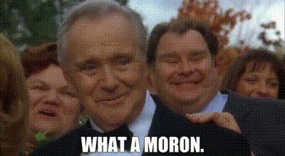 A Man In A Suit And Tie Is Smiling In Front Of A Group Of People . GIF