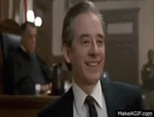 A Man In A Suit And Tie Is Smiling In Front Of A Judge In A Courtroom . GIF