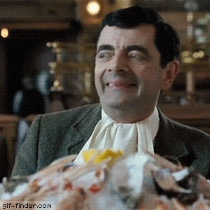 A Man In A Suit And Tie Is Smiling In Front Of A Pile Of Food With Gif-Finder.com In The Corner GIF