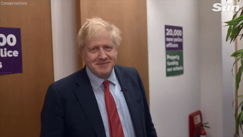 A Man In A Suit And Tie Is Smiling In Front Of A Sign That Says Conservatives On It GIF