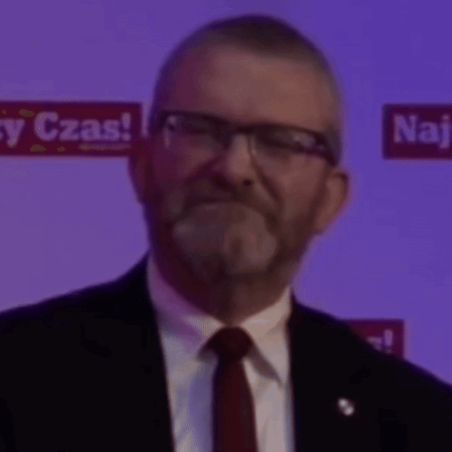 A Man In A Suit And Tie Is Smiling In Front Of A Sign That Says " Czas " GIF
