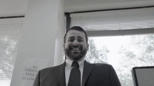 A Man In A Suit And Tie Is Smiling In Front Of A Sign That Says No Person Effect Allow GIF