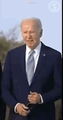 A Man In A Suit And Tie Is Smiling While Holding A Cell Phone . GIF