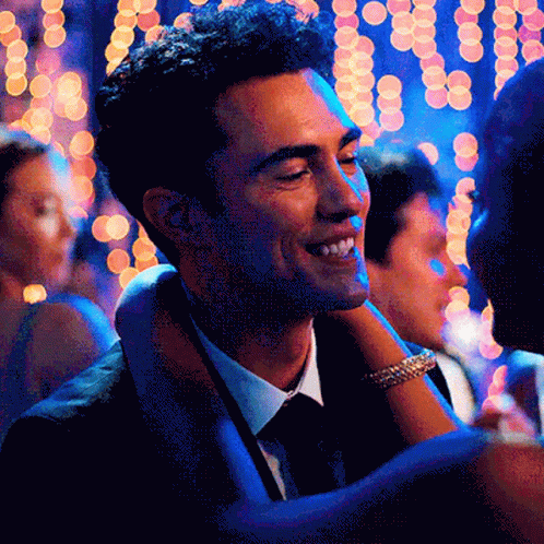 A Man In A Suit And Tie Is Smiling While Holding A Woman 'S Arm GIF