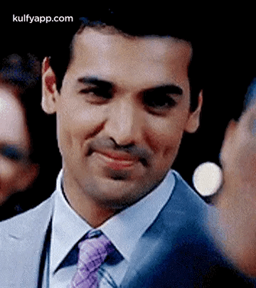 A Man In A Suit And Tie Is Smiling While Looking At The Camera . GIF