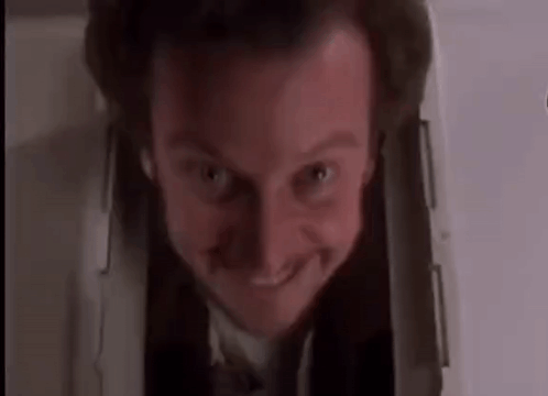 A Man In A Suit And Tie Is Smiling While Looking Out Of A Hole In The Wall . GIF