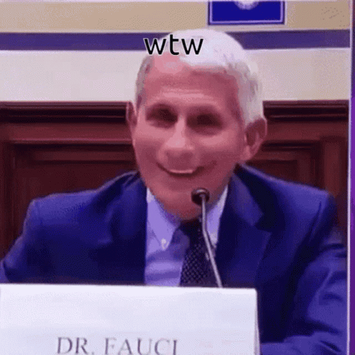 A Man In A Suit And Tie Is Smiling While Sitting At A Table With A Microphone . GIF