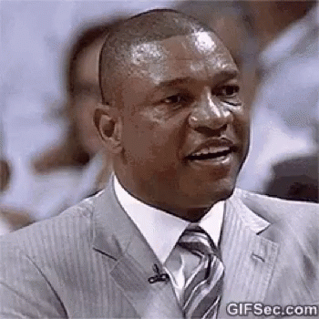 A Man In A Suit And Tie Is Smiling While Sitting In A Crowd . GIF