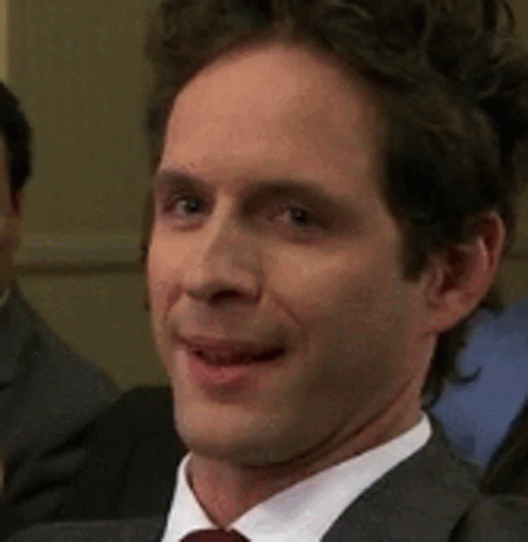 A Man In A Suit And Tie Is Smiling While Sitting In A Room . GIF
