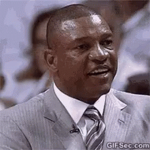 A Man In A Suit And Tie Is Smiling While Sitting In Front Of A Crowd . GIF