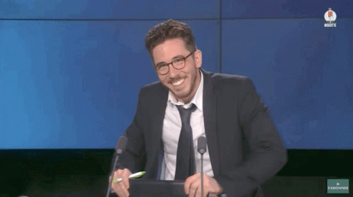 A Man In A Suit And Tie Is Smiling While Sitting In Front Of A Microphone GIF