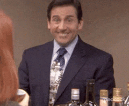 A Man In A Suit And Tie Is Smiling While Standing In Front Of A Bar With Bottles Of Alcohol . GIF