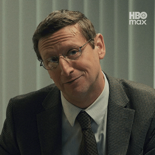 A Man In A Suit And Tie Is Smiling With A Hbo Max Logo In The Background GIF