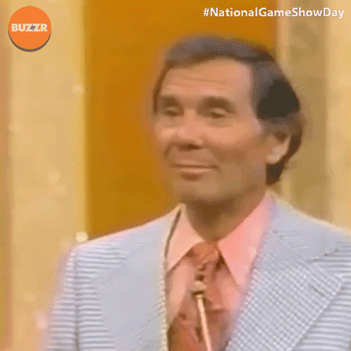 A Man In A Suit And Tie Is Smiling With The Words National Game Show Day Below Him GIF