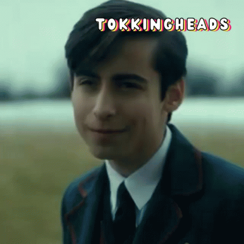 A Man In A Suit And Tie Is Smiling With The Words Tokingheads Written Above Him GIF