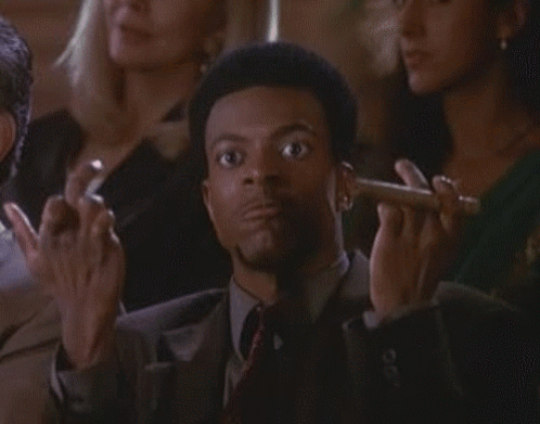 A Man In A Suit And Tie Is Smoking A Cigar In A Crowd Of People GIF