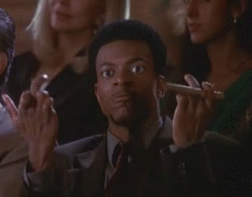 A Man In A Suit And Tie Is Smoking A Cigar In Front Of A Crowd . GIF